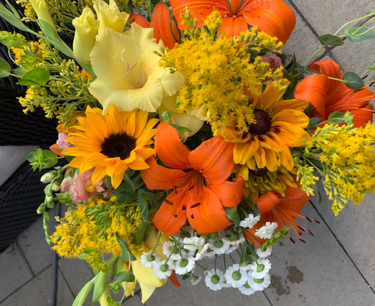 A vibrant bouquet of fresh flowers featuring sunflowers, lilies, and other summer blooms with greenery.